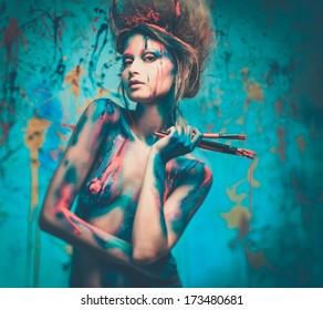 Young woman muse with creative body art and hairdo holding paint brushes 
