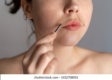 A young woman with a mustache tries to remove the hair over her lip with tweezers. The concept of getting rid of unwanted facial hair. Close up