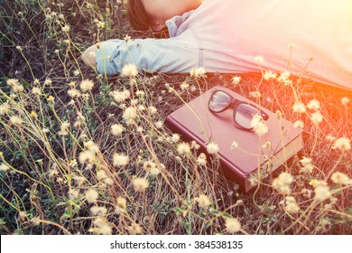 Young Woman Napping On The Dandelion Field After Reading Book Put Out Glasses On The Book