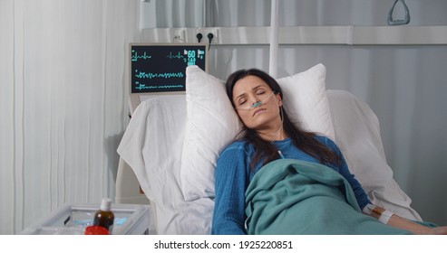 Young Woman With Nasal Oxygen Tube Sleeping In Hospital Bed. Portrait Of Sick And Tired Female Patient Unconscious Lying In Bed Wearing Breathing Tube In Hospital Ward