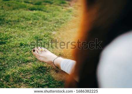 Young woman in the nature, sitting on the grass, camomile flowers on her feet.