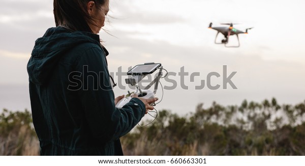Young woman\
navigating a flying drone with remote control. Woman in countryside\
flying drone and taking\
pictures.