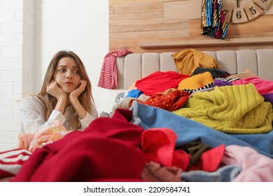 Young Woman Near Bed With Pile Of Clothes In Messy Room. Fast Fashion Concept