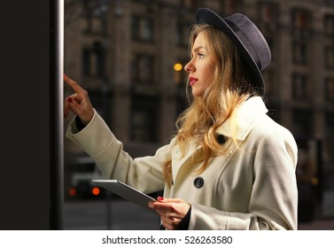 Young Woman Near Digital Screen In Street At Evening Time