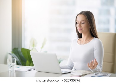 Young Woman Near The Laptop, Practicing Meditation At The Office Desk, In Front Of Laptop, Online Yoga Classes, Taking A Break Time For A Minute, Healing From Paperwork And Laptop Radiation