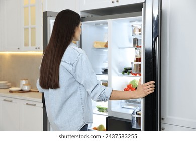 Young woman near modern refrigerator in kitchen - Powered by Shutterstock