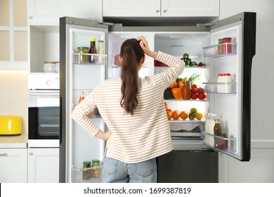 Young woman near open refrigerator in kitchen, back view