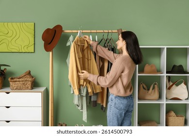 Mujer joven cerca del estante con ropa moderna en vestidor