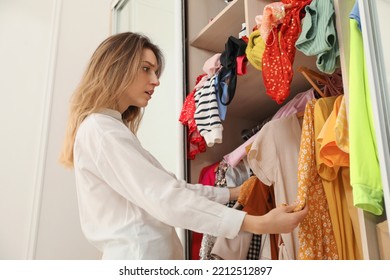 Young Woman Near Wardrobe With Different Clothes Indoors. Fast Fashion Concept