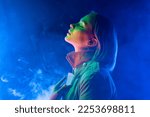 Young woman in neon multi-colors light on smoke, steaming background. Millennial enigmatic futuristic lady in fashion trench coat, stylish outfit 