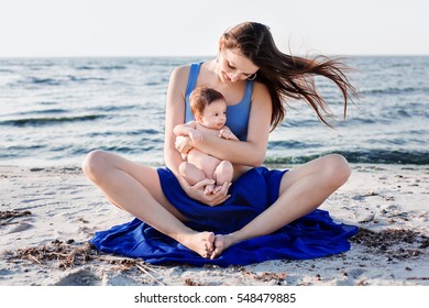 Young woman with newborn baby practicing yoga at beach on the sunset