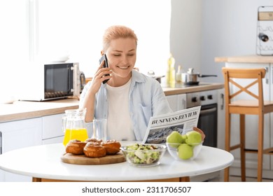 Young woman with newspaper talking by mobile phone in kitchen - Powered by Shutterstock