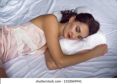 Young Woman In A Nightgown Lying In A White Bed On The Pillow