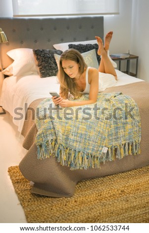 Young woman in nightwear text messaging on mobile phone in bed