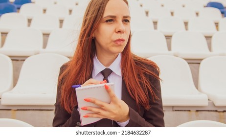 Young Woman With Notepad, Pen Sitting On Stadium Bleachers Alone. Female Journalist Writing Down Notes During Sports Training At Street Stadium