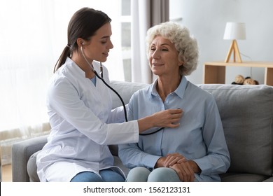 Young woman nurse doctor gp holding stethoscope examining old senior 60s grandma patient check heartbeat at homecare checkup medical visit at home hospital, older people cardiology healthcare concept