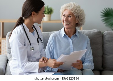 Young woman nurse doctor wear medic uniform consult happy old grandmother patient hold papers show medical test result offer healthcare consent insurance contract form at home hospital concept