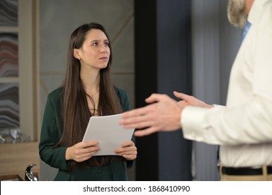 Young Woman, Office Worker Communicates With A Senior Very Tall Colleague, Looks Up At Him