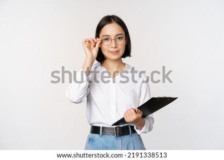 Young woman, office worker manager in glasses, holding clipboard and looking like professional, standing against white background