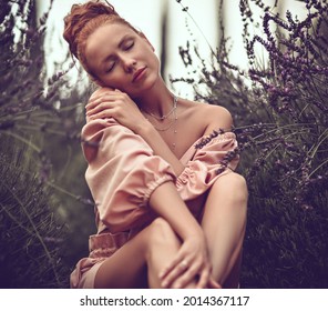 Young Woman In Off-shoulder Jumpsuit Or Dress Sits In The Middle Of Field With Her Eyes Closed, Feeling Aroma, The Fragrance Of Wild Flowers. Tropical Background. Summer Vibes