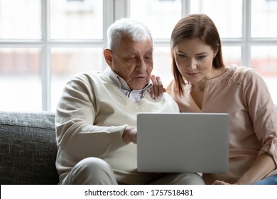 Young Woman And Older Man Using Laptop Together, Looking At Screen, Sitting On Couch At Home, Mature Father Asking Questions To Grownup Daughter, Studying To Use Computer, Pointing At Screen