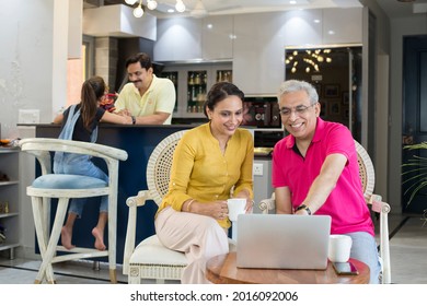 Young Woman And Older Man Using Laptop Together, Looking At Screen, Sitting On Chair At Home.