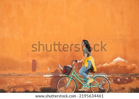 Young woman on a bicycle. Beautiful Hispanic teenage girl riding a bicycle with a large wall of colonial architecture as a background.