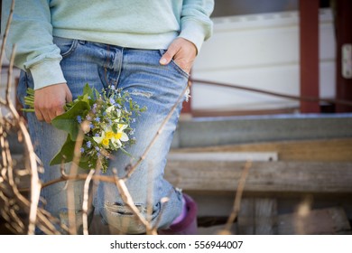 Young woman on blue jeans holding a beautiful garden flowers in her hand. Summer bouquet in girl's hand. Outdoor. Spring garden present. Sunlight in the garden. Woman with bunch of flowers. Farm