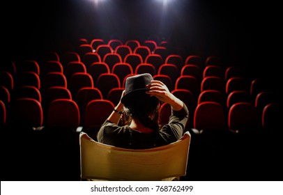 Young Woman On Director's Chair On Stage, In Front Of Empty Seats