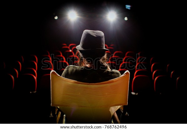 Young woman on director\'s chair on stage, in front\
of empty seats