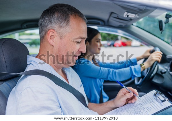 Young woman on a driving test with her\
instructor. Learning to drive a car. Driving school. Instructor of\
driving school giving exam while sitting in\
car