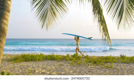 Young woman on fun surfing trip in Barbados carries a surfboard on her head while walking on the golden-lit tropical beach. Female surfer walks along the white sand beach with a surfboard on her head. - Powered by Shutterstock