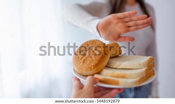 Young woman on gluten free diet is saying\
no thanks to toast. A woman on a gluten free diet is saying no\
thanks to toast. Woman refusing to eat white\
bread