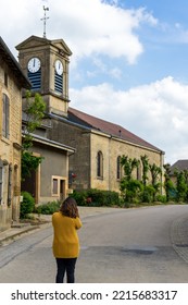 Young Woman On Her Back In The Middle Of A Road In A Typical French Village, With The Church Tower In The Background. High Quality Photo