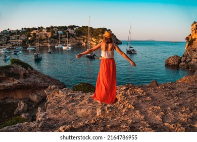 Young woman on holiday with her arms stretched out happily looking at the landscape, in the cove of Portal Vells, island of Palma de Mallorca, Spain.