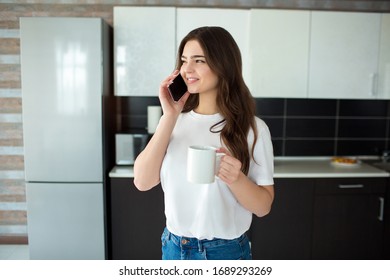 Young woman on kitchen during quarantine. Talking on smartphone and smile. Modern technologies during quarantine period. Working online.