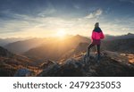 Young woman on mountain peak and beautiful mountain valley in haze at colorful sunset in autumn. Dolomites, Italy. Sporty girl, mountain ridges in fog, orange grass, trees, golden sun in fall. Hiking