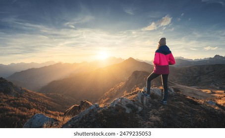 Young woman on mountain peak and beautiful mountain valley in haze at colorful sunset in autumn. Dolomites, Italy. Sporty girl, mountain ridges in fog, orange grass, trees, golden sun in fall. Hiking - Powered by Shutterstock