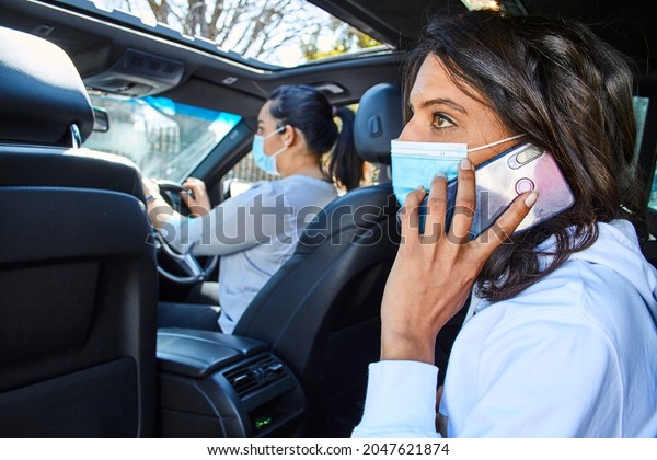 A young woman is\
on the phone while in the back seat of a taxi wearing a face mask\
during the pandemic