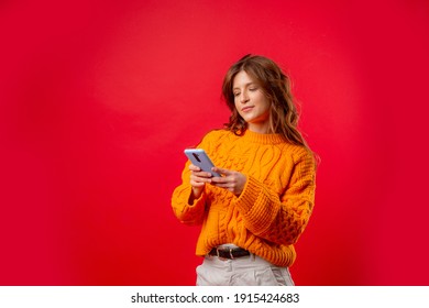 A Young Woman On A Red Background Is Holding A Mobile Phone Typing A Message