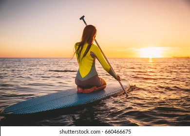 Young woman on stand up paddle board on a sea with warm summer sunset colors. Relaxing on ocean