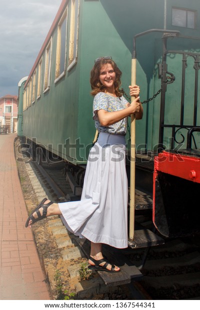 A young woman on the steps of the car. The girl  in the\
departing retro train Vintage cars in the style of the early 20th\
century 