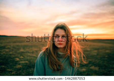 Young woman on sunset in field with fluttering hair