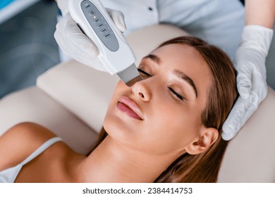 Young woman on ultrasound facial beauty treatment. Peeling nose facial cleaning pampering procedure closeup. Cosmetologist in gloves using beauty equipment - Powered by Shutterstock