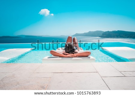 Young woman on vacation at Santorini, women at the swimming pool looking out over the Caldera ocean of Santorini, Girl at the infinity pool Oia Santorini Greece