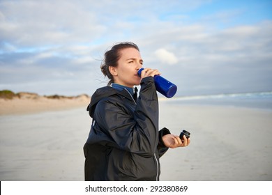 Young Woman On A Winter Beach Drinking From Her Water Bottle