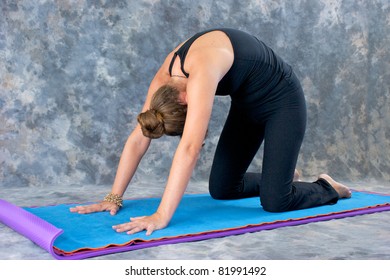 Young woman on yoga mat in  Yoga posture Marjaryasana or cat pose against a grey mottled background .