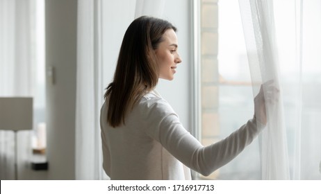 Young Woman Open Curtains At Home Or Hotel Look In Window Distance Thinking Or Dreaming, Happy Millennial Female Admire View, Feel Optimistic And Positive, Welcome New Sunny Day, Early Morning