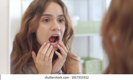 Young woman with opened mouth checking teeth in mirror in home bath room. Brunette woman looking mouth, teeth and smile front bathroom mirror. Teeth care, beauty and health concept