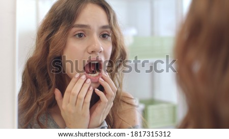 Young woman with opened mouth checking teeth in mirror in home bath room. Brunette woman looking mouth, teeth and smile front bathroom mirror. Teeth care, beauty and health concept